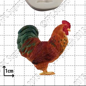 May include: A silicone mold for making a rooster cake topper. The mold is white and shows the detailed shape of a rooster with a red comb and wattles. A painted rooster cake topper is shown next to the mold.