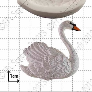 May include: A white silicone mold of a swan with a 1 cm scale bar. The mold is designed to create a 3D swan cake decoration.