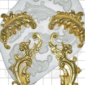 May include: A silicone mould for making decorative cake accents. The mould features four designs, including two ornate scrolls and two leaf-shaped designs. The mould is shown with the designs filled with gold-coloured fondant.