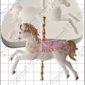 Puede incluir: Un caballo de carrusel blanco con una silla de montar rosa y ribetes dorados. El caballo tiene una crin y una cola doradas y está decorado con rosas rosas. El caballo está unido a un poste dorado con un diseño en espiral. La imagen incluye una barra de escala con la medida de 1 cm.