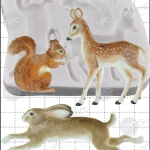 May include: A silicone mold featuring a squirrel, a deer, and a rabbit. The squirrel is brown and orange, the deer is tan with white spots, and the rabbit is brown. The mold also has the outline of other animals.