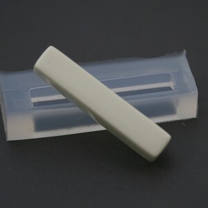 May include: A white rectangular mold for making resin crafts. The mold is made of clear silicone and has a rectangular opening. A white rectangular resin piece is sitting on top of the mold.