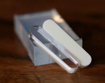 May include: Two clear glass nail files, one with a white plastic cover, are lying on a wooden surface.