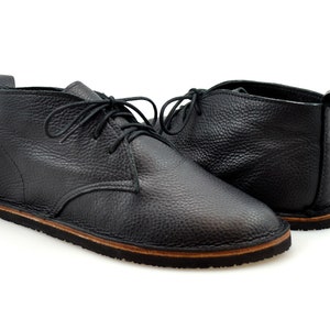 Puede incluir: Un par de botines de cuero negro con cordones. Los botines tienen una suela de goma marr&oacute;n.