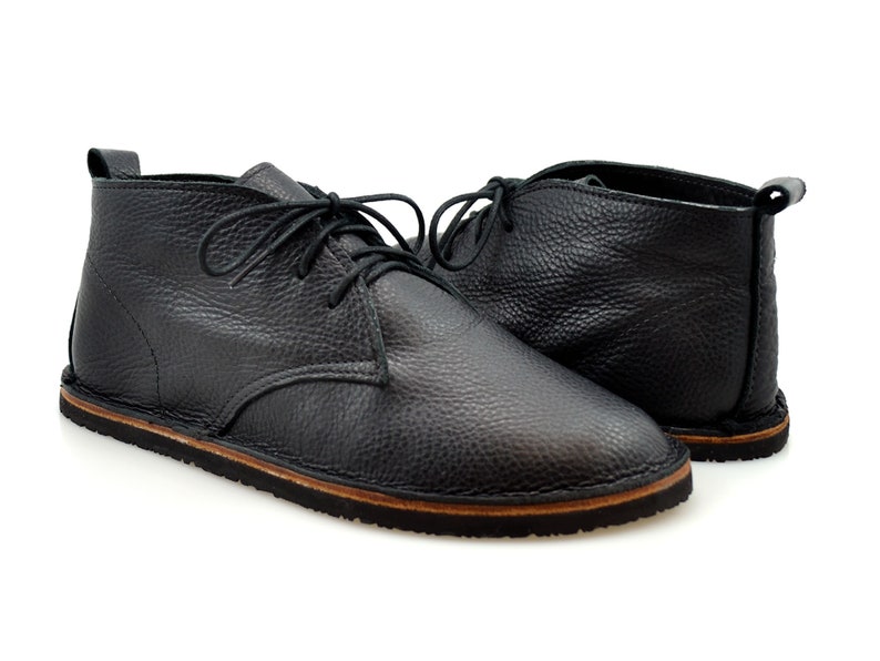 Puede incluir: Un par de botines de cuero negro con cordones. Los botines tienen una suela de goma marr&oacute;n.
