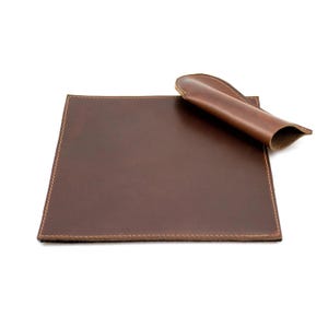 May include: A brown leather desk mat with a matching brown leather pen holder. The mat has a stitched edge.