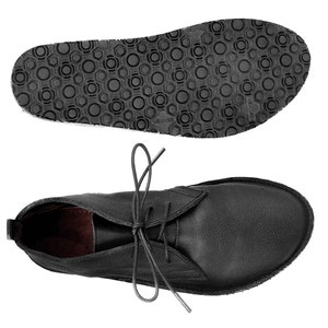 Puede incluir: Botas de tobillo de cuero negro con cordones. Las botas tienen una suela de goma texturizada.