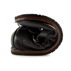 Puede incluir: Primer plano del interior de un zapato de cuero negro con suela de cuero marr&oacute;n.