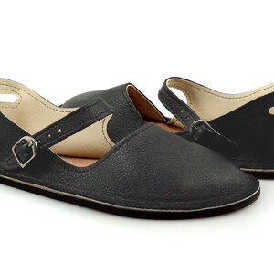 May include: Black leather slip-on shoes with a buckle strap and an open back.