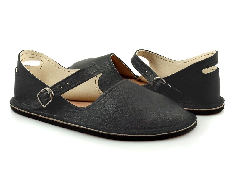 May include: Black leather slip-on shoes with a buckle strap and an open back.