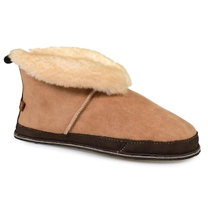 May include: Tan suede slipper boot with a dark brown sole and trim. The boot features a soft, cream-colored shearling lining and a small loop at the back. A cozy and comfortable footwear option for indoor wear.