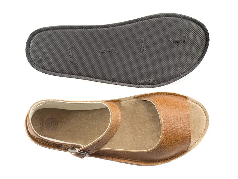 Puede incluir: Sandalias de cuero marr&oacute;n claro con cierre de hebilla y plantilla blanca. Las sandalias tienen una suela texturizada.