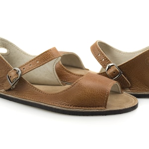 Puede incluir: Un par de sandalias de cuero marr&oacute;n con cierre de hebilla y puntera abierta. Las sandalias tienen un dise&ntilde;o sencillo y est&aacute;n hechas de un cuero suave y c&oacute;modo.