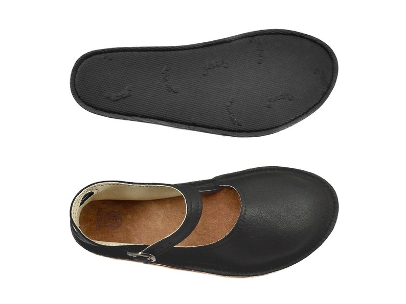 May include: Black leather ballet flats with a strap across the foot and a buckle closure. The shoes have a brown leather insole and a black rubber outsole.