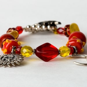 May include: A red, yellow, and silver bracelet with a sun and moon charm. The bracelet is made of glass beads and metal.