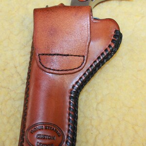 May include: A brown leather holster with black lacing along the edges, featuring a stamped logo that reads Rohn Stearns Custom Leather. A small revolver with a polished metal frame and wood grain grip is partially inserted into the holster.