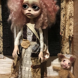 May include: A handcrafted doll with a pale face, large eyes, and pink curly hair. The doll wears a patchwork dress with a beige shoulder bag. A small stuffed bunny lies on the floor nearby. The setting appears to be a miniature room.