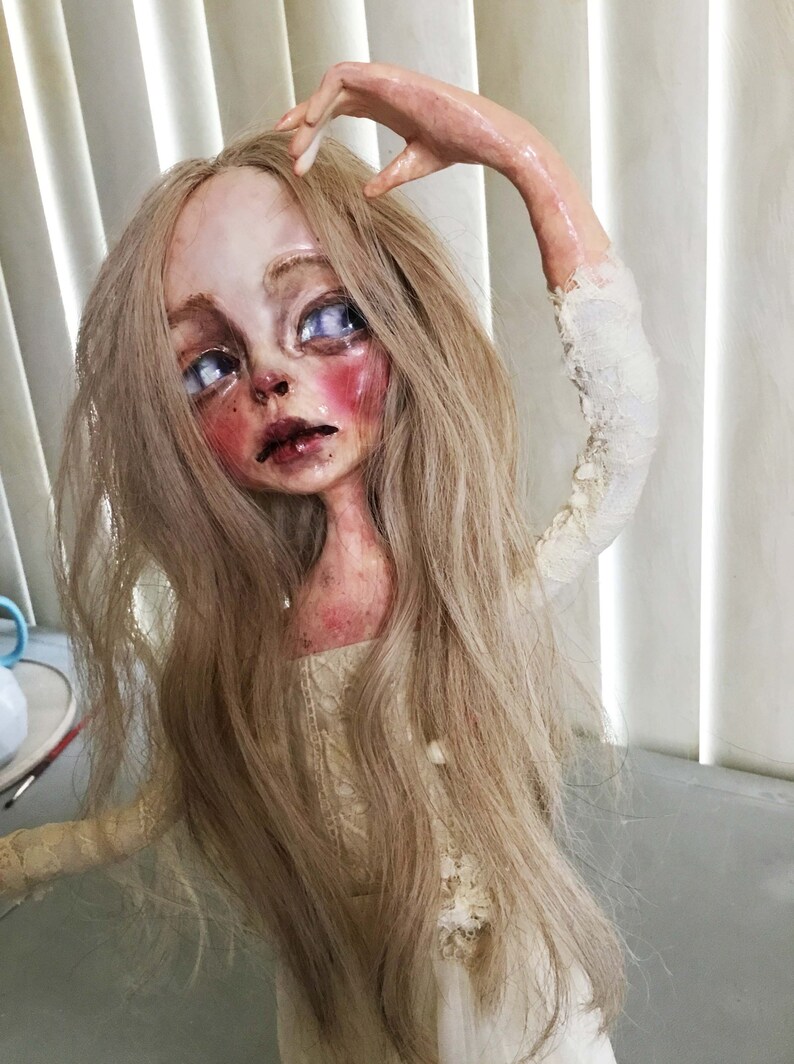 May include: A porcelain doll with long blonde hair, wearing a white lace dress. The doll has a pale complexion, blue eyes, and rosy cheeks.