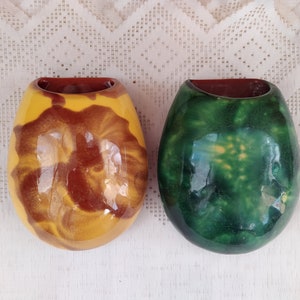Könnte beinhalten: Zwei Keramik-Wandvasen, eine mit einer gelben und braunen Marmorierung und die andere mit einer grünen und weißen Marmorierung.