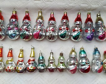 May include: A collection of 25 vintage Christmas baubles, mostly depicting snowmen, with silver, red, and blue accents. The baubles are made of glass and have a variety of designs.