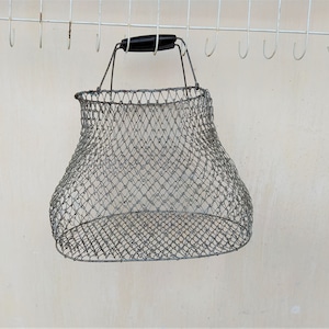 Puede incluir: Una cesta de alambre de malla plateada con un asa negra colgada de una pared blanca con ganchos.