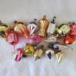May include: A collection of vintage Christmas ornaments in various shapes and colors, including gold, silver, pink, and orange. The ornaments have a reflective, glossy finish and are arranged on a white surface.