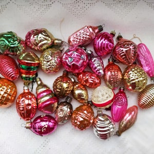 May include: A collection of vintage glass Christmas ornaments in various colors, including pink, red, green, gold, and silver. The ornaments are decorated with different patterns and designs, including stars, stripes, and geometric shapes.