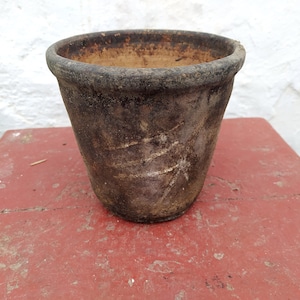 May include: A brown terracotta flower pot with a rough, textured surface. The pot is slightly weathered and has a worn appearance.