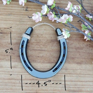 Puede incluir: Una herradura de plata con un acabado r&uacute;stico, que mide 11,4 cm de ancho y 12,7 cm de alto. Est&aacute; atada con una cuerda de yute natural.
