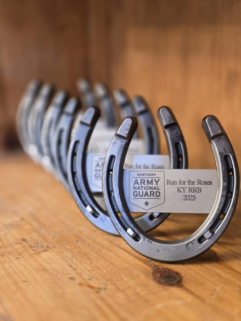 May include: A row of silver horseshoes with a white label attached to the front horseshoe. The label reads "Run for the Roses Kentucky Army National Guard KY RRB 2025".