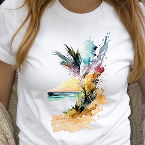Op de afbeelding: Wit T-shirt met een aquarelontwerp van een palmboom op een strand met een zonsondergang op de achtergrond.