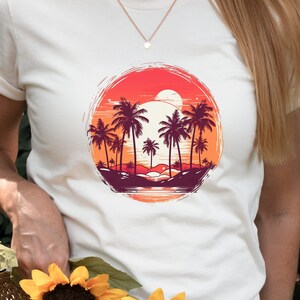 May include: White t-shirt with a graphic of palm trees and a sunset in a circle. The sunset is orange, red, and yellow. The palm trees are dark purple and green.