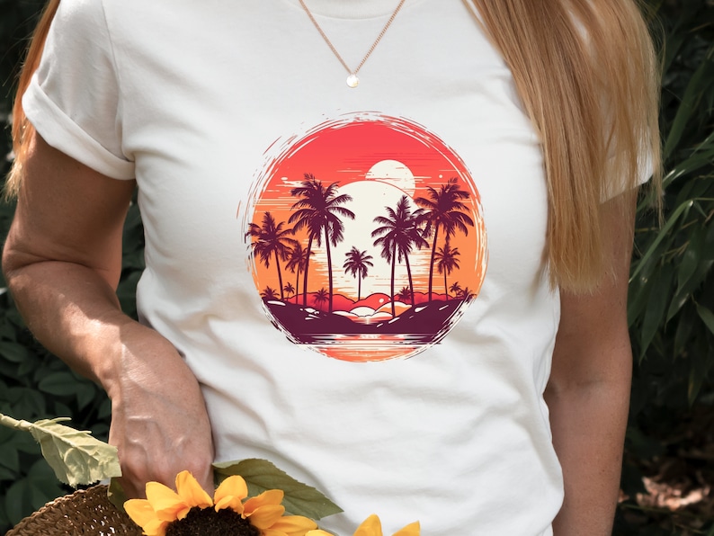 May include: White t-shirt with a graphic of palm trees and a sunset in a circle. The sunset is orange, red, and yellow. The palm trees are dark purple and green.