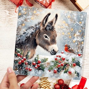 Biglietto di Natale con asino e pettirosso, scena innevata, bacche di agrifoglio, luci fatate, paesaggio invernale festoso, auguri di Natale per la famiglia, gli amici 2025