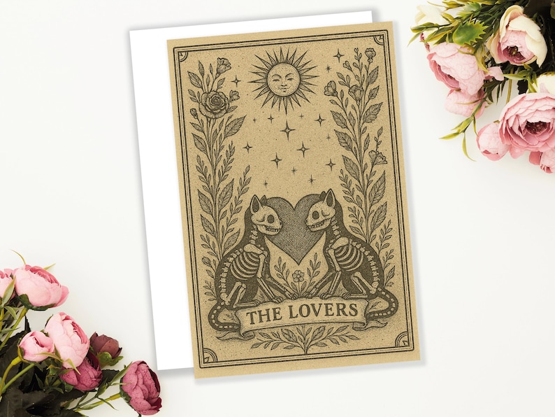May include: A tarot card illustration featuring two skeleton cats facing each other, with a heart between them. The card has a sun, stars, and floral elements. The text "THE LOVERS" is on a banner at the bottom.