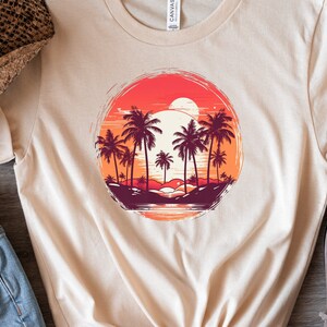 May include: A beige t-shirt with a graphic print of a sunset over a beach with palm trees. The graphic is in a circle with a distressed look.