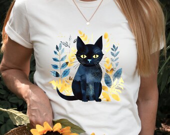May include: White t-shirt featuring a watercolor illustration of a black cat with yellow eyes, surrounded by blue and yellow foliage. The cat is sitting upright. The shirt is made of a soft material.