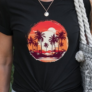 May include: Black t-shirt with a graphic of palm trees and a sunset in a circle. The graphic is in shades of orange, red, and yellow.