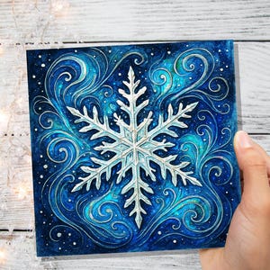 May include: A square, winter-themed artwork featuring a detailed, white snowflake design at the center. The snowflake is set against a deep blue background with swirling, stylized water and snow effects. The artwork is held by a hand.