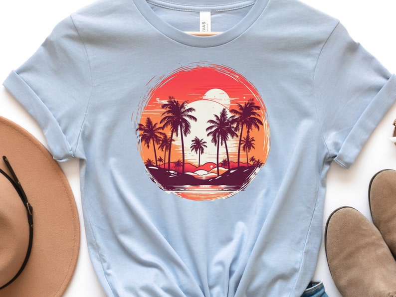 May include: Light blue t-shirt with a graphic print of palm trees and a sunset in a circle. The graphic is in shades of orange, red, and purple.