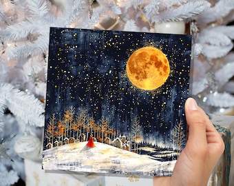May include: A square art print depicts a winter landscape under a starry night sky. A large, glowing orange moon dominates the scene. A figure in a red cloak stands on a snow-covered hill, with trees and small buildings in the background.