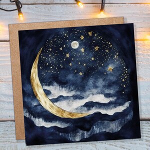 May include: A greeting card featuring a watercolour illustration of a crescent moon and stars against a dark blue background. The moon is gold and the stars are gold with a white centre. The background is a dark blue with white clouds.
