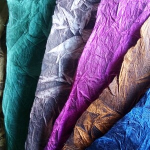 May include: A collection of six sheets of textured, crinkled paper arranged in a vertical row. The colors include olive green, emerald green, charcoal gray, vibrant purple, golden brown, and deep blue, each featuring a distinct wrinkled surface.