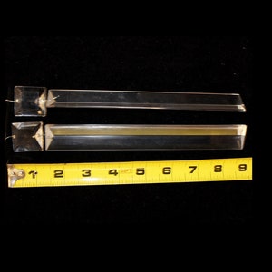 May include: Two clear glass prism crystal pendants with square ends. The prisms are approximately 4 inches long. A yellow measuring tape is in the background.