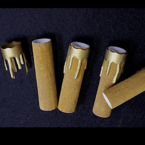 May include: Five gold-painted candle holders with a textured surface. The candle holders are in various positions on a black surface.