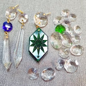 May include: An assortment of clear and colored crystal chandelier parts. Includes faceted teardrops, round and oval crystals, a blue crystal, and a green crystal. A green and white star-shaped pendant is also present.