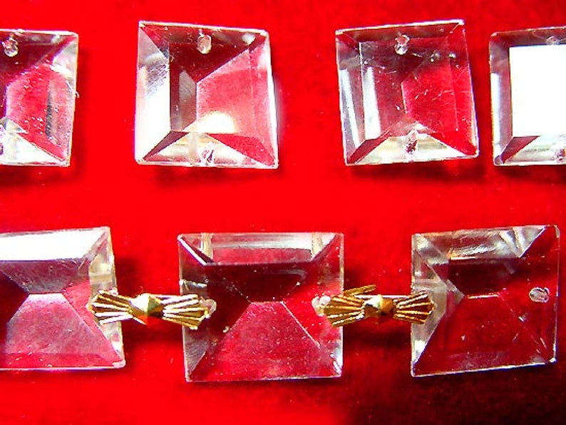 May include: A set of clear glass square crystals with gold metal connectors. The crystals are faceted and have a hole in the centre. The connectors are in the shape of a bow.