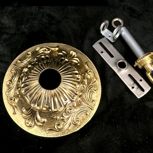 May include: A gold-colored ceiling canopy with ornate floral detailing, a mounting bracket, and a threaded rod with a hook. The components are for a light fixture.
