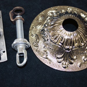 May include: A silver ceiling fixture kit with a decorative, ornate, round, metal canopy. The kit includes a metal mounting plate, a threaded rod, and a hook.