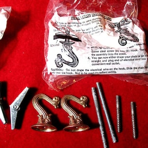 May include: A close-up of a package containing two decorative gold hooks, four screws, and two metal clips. The package includes instructions for installing the hooks. "INVALLATION INSTR" is printed on the package.
